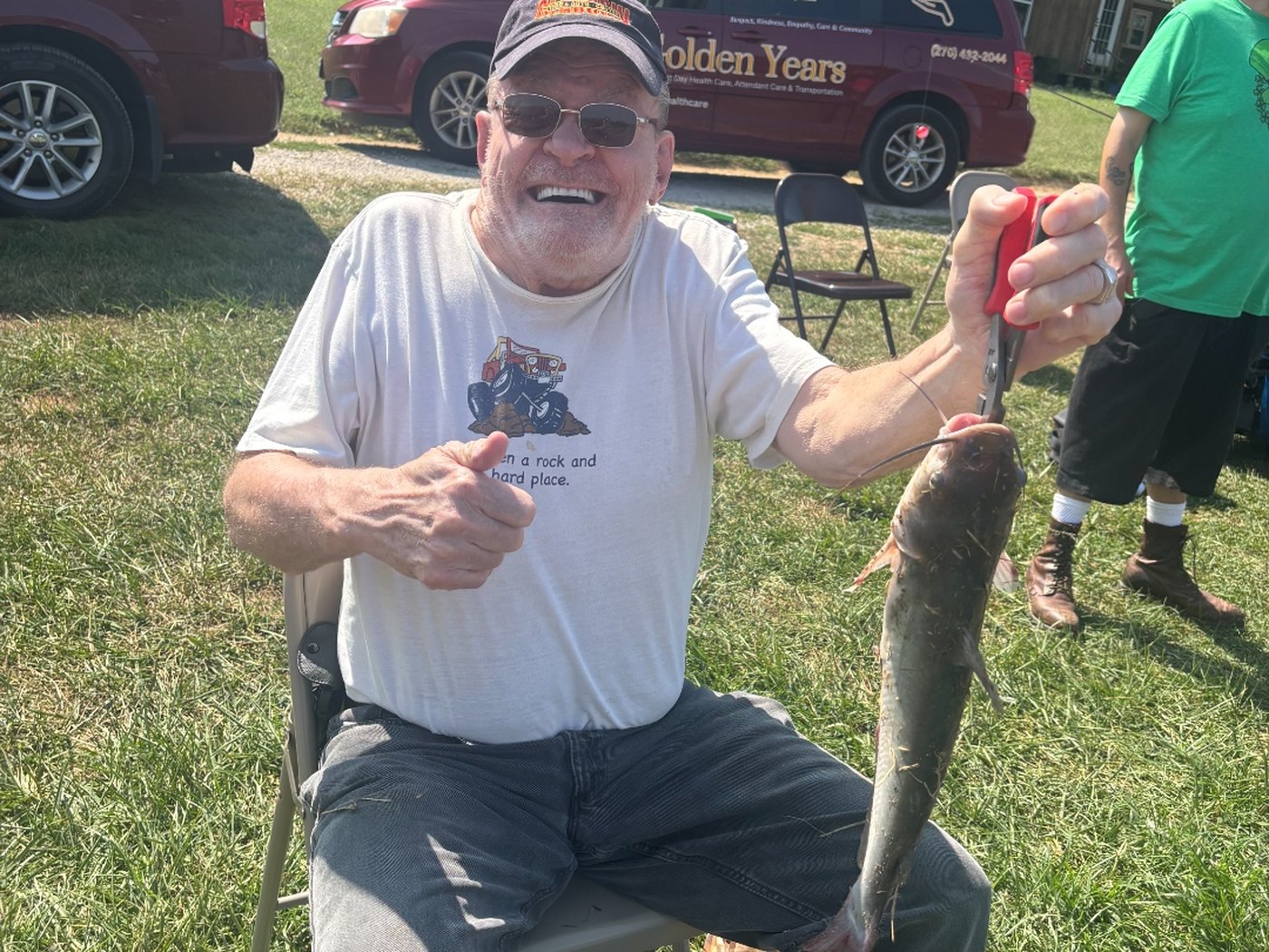 A Golden Years member giving a thumbs-up with his catch on a community outing, branded van behind him